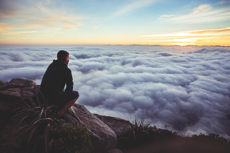person crouches on ledge of rocky bluffs look at billowing clouds, sunset in solitude 4k