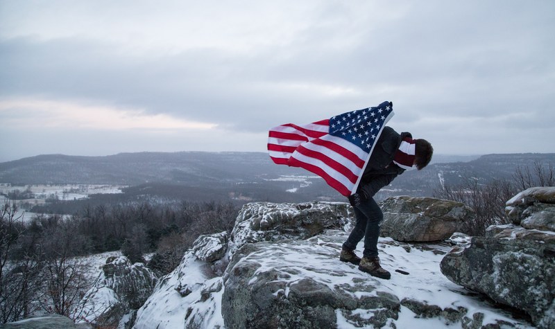 a climber holds the american flag while standing on the peak of a snowy mountain, american flag on a mountain 4k