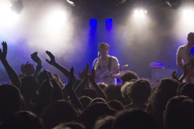 a small crowd at a concert with a band member playing the guitar in blue lights and smoke, front row audience 4k