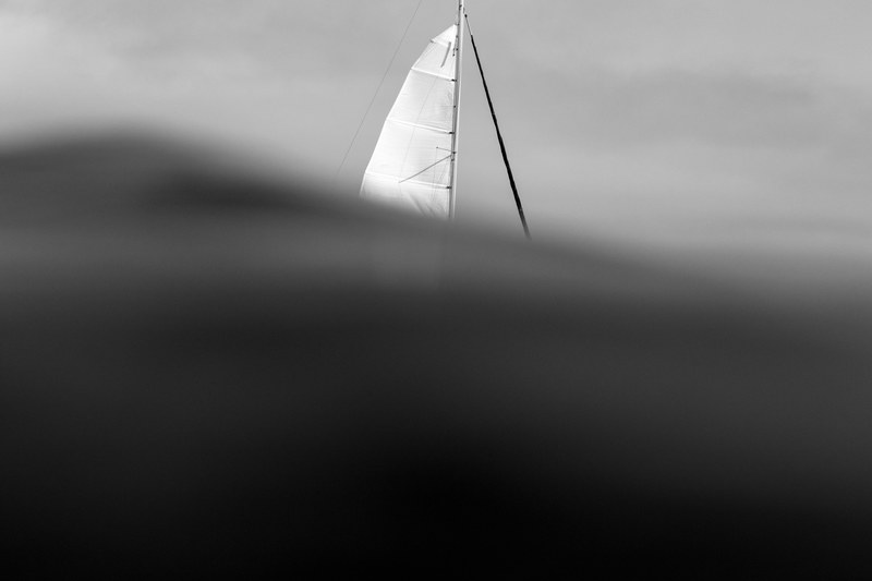 a gray image taken behind a wave with a glimpse of a nearby sailboat, _sailboat from behind wave 4k