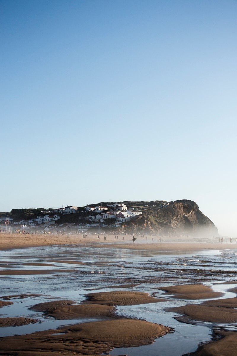 people at the sand beach below white houses on a rocky hill in praia do monte clrigo, white houses above sand beach 4k