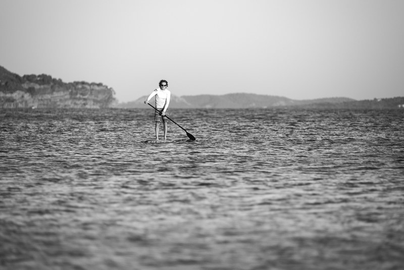 a man with curly hair standing on a paddleboard in the sea steering with his oar, paddleboarder enjoying the water 4k