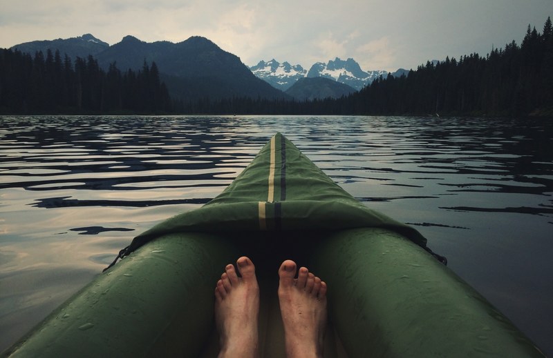 the view of a persons feet and the front of their canoe on a lake, calm lake 4k