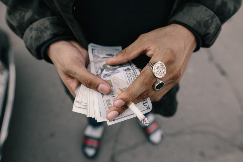 close up of a mans hands holding a bundle of dollar bills and a cigarette, doing business in the street 4k