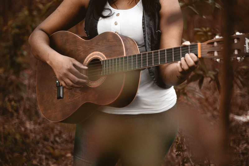a woman playing acoustic guitar with leaf covered ground in the background, acoustic guitar on the forest floor 4k