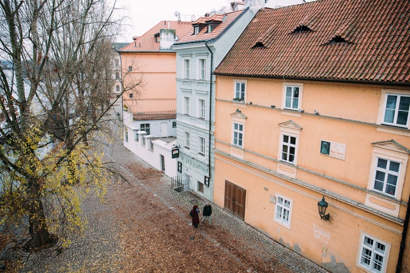 aerial view of an urban street lined with colorful houses and a couple walking on the sidewalk next to a cobblestone street, cobblestone street and houses 4k