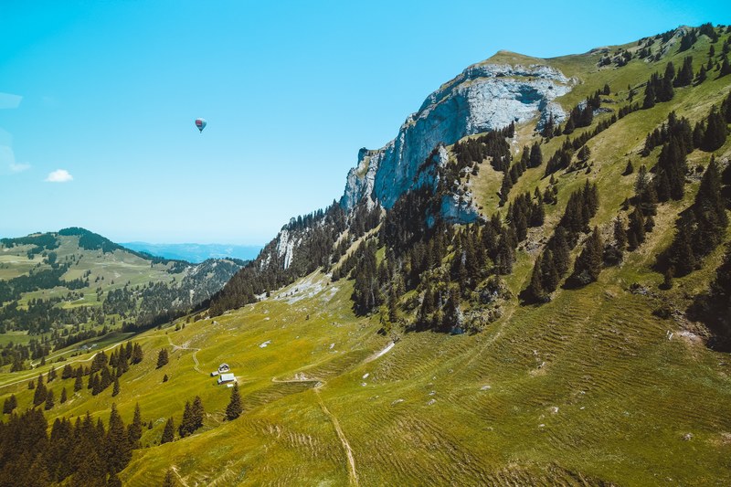 a hot air balloon in the air over a green mountain slope, hot air balloon over green slopes 4k