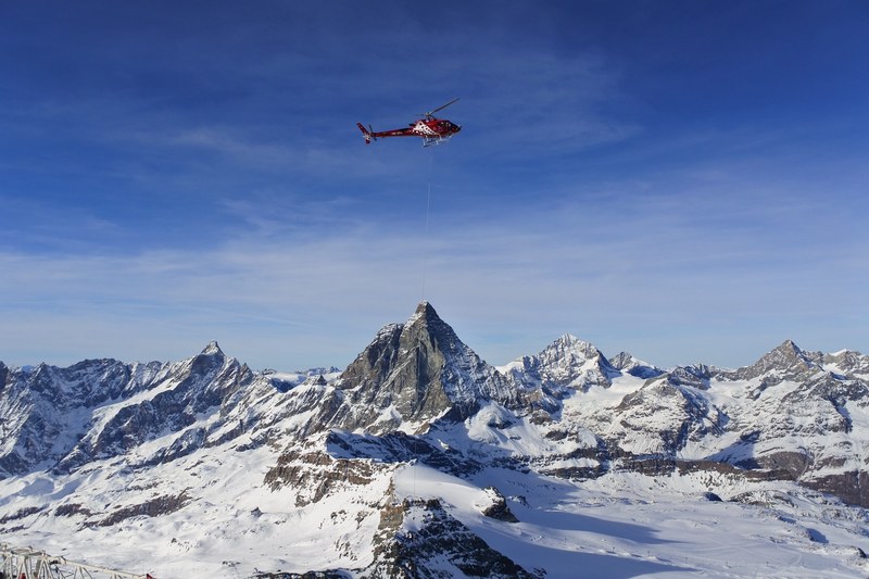 a rescue helicopter with a rescue hoist in the air above snowy mountains, beautiful december day in a swiss resort zermatt 4k