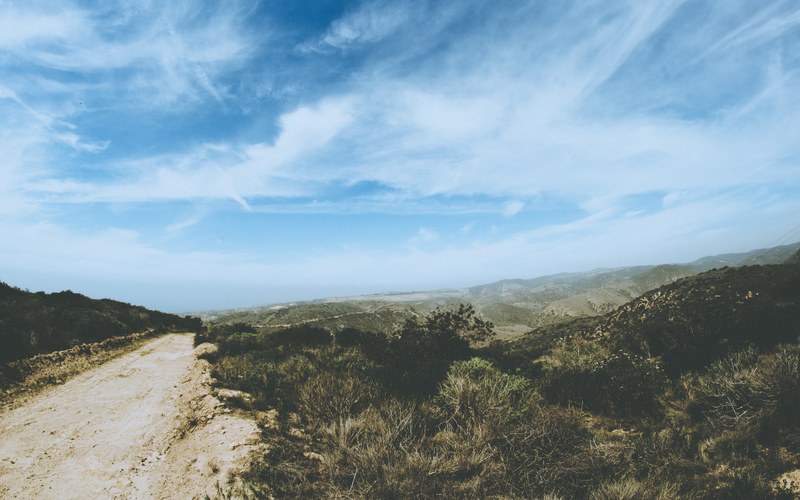 a pale shot of a dirt road on the edge of hilly grasslands, road by the dry grasslands 4k