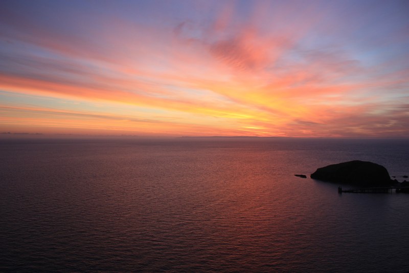 orange glow of the setting sun in the sky over a dark rock in a vast sea, calm sea lundy sunset 4k