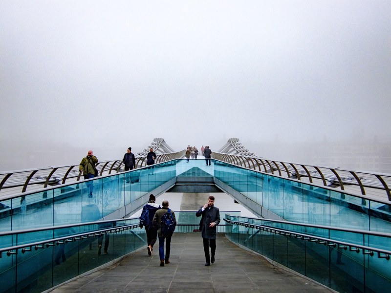 fog slowly envelops the steel and glass structure of the millennium bridge as people use it for commute, fog across the busy millennium bridge 4k