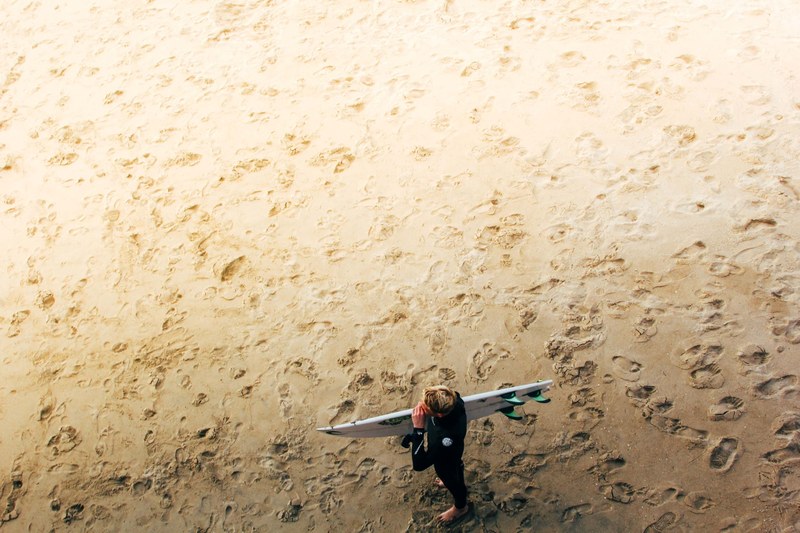 surfer standing on the sand beach riddled with footprints at manhattan beach pier, manhattan beach pier surfer 4k