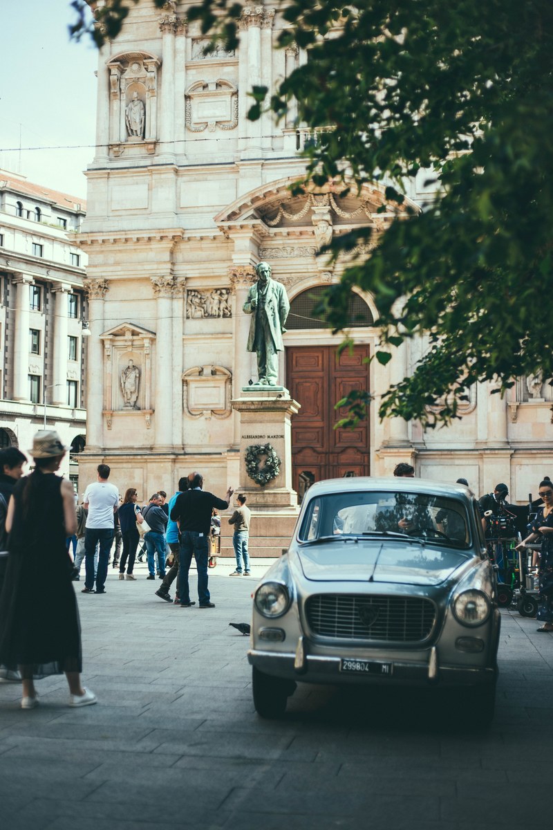 old vintage white car parked on the crowded square in front of the statue and an old building in milan, vintage car parked on the square in milan 4k