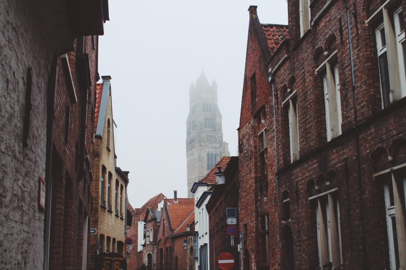 a street in bruges with brick houses and a church covered in fog in the background, foggy day in brugge 4k