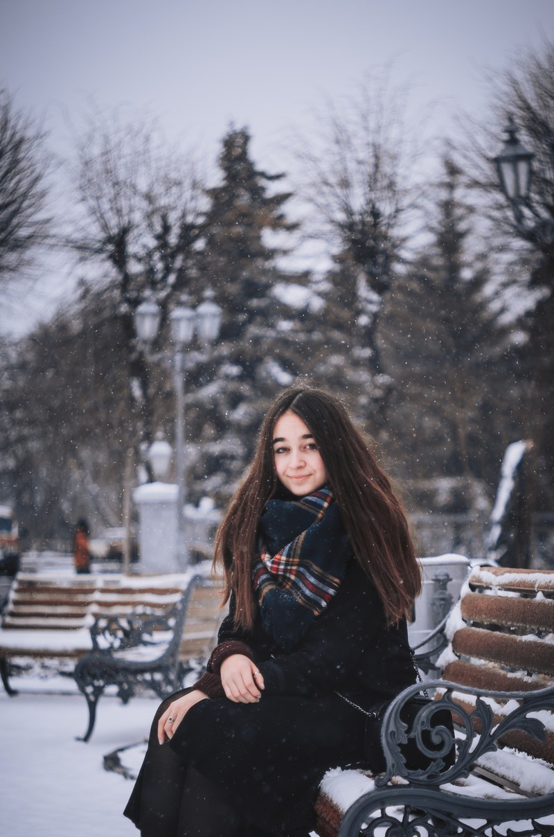 a smiling woman in a scarf sits on a park bench in the snow, woman on park bench 4k