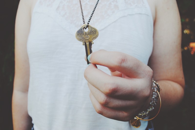 a person holding a key with the word fearless etched on it, fearless key necklace 4k