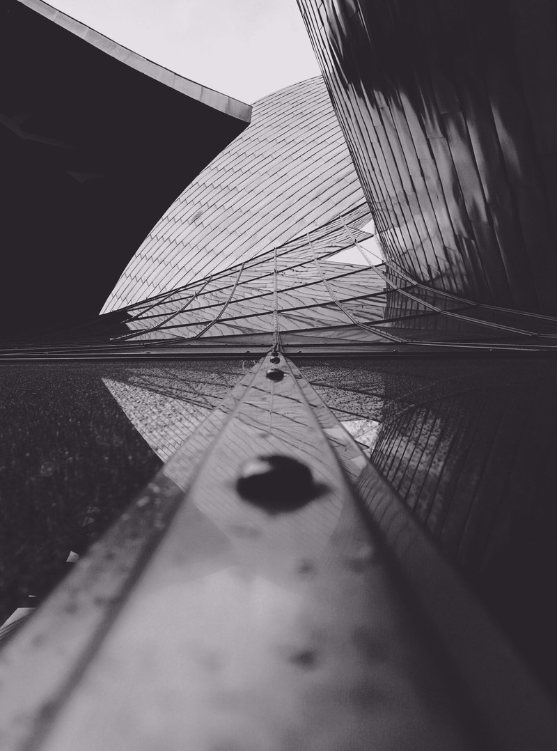 a low angle shot of a modern building facade of metal and glass, monochrome guggenheim bilbao 4k