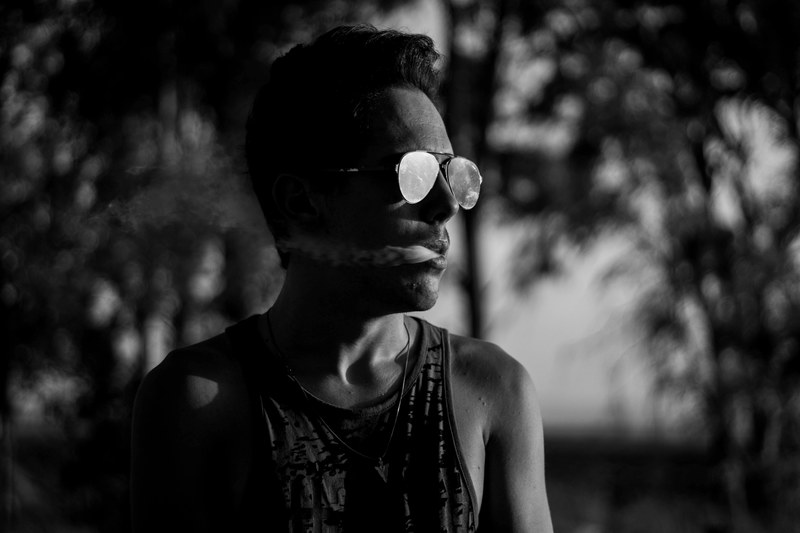 a man in sunglasses in black and white exhales smoke while looking to the side, man exhaling smoke 4k