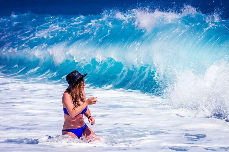 woman in a swimsuit with a hat about to be splashed by the wave at lalaria beach, lalaria beach woman 4k