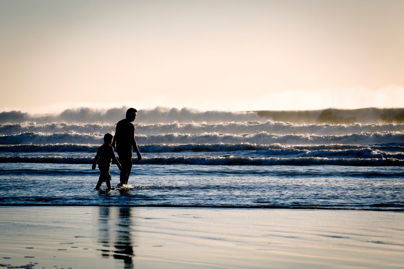 father and son wading on an ocean beach, before the breakers 4k