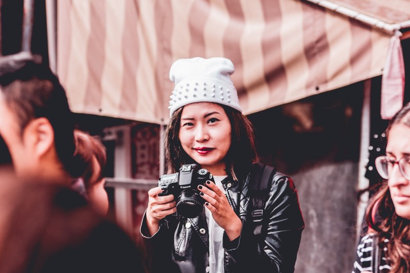 smirking photographer in a white hat and leather jacket holds a camera in a kyoto market, smirking photographer in kyoto 4k