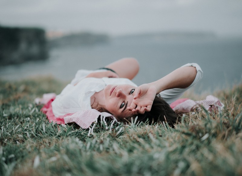 woman lying in the grass looking at the camera at bondi beach, cliffs at sunset 4k