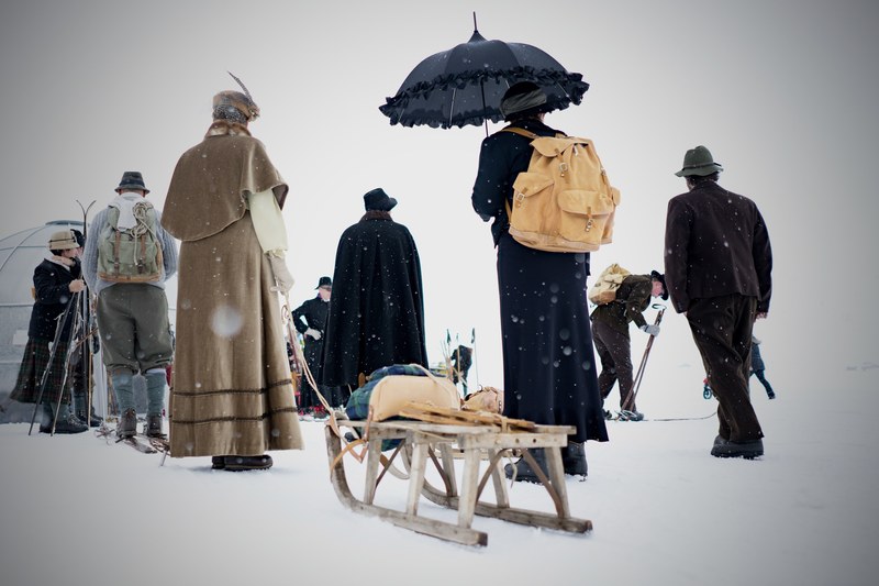 people in coats with a sled skies an umbrella and backpacks are traveling through snowfall, snowy vintage trek 4k