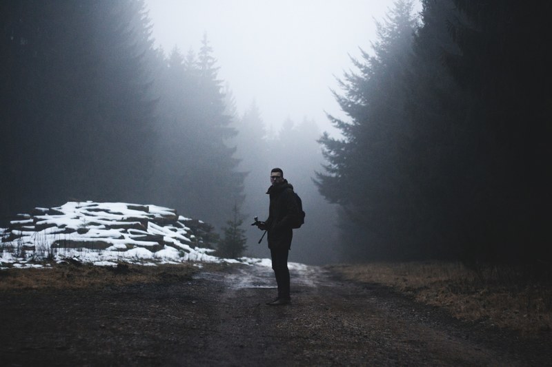 man stands on a path surrounded by evergreen trees and slight dusting of snow, man standing on dirt path 4k