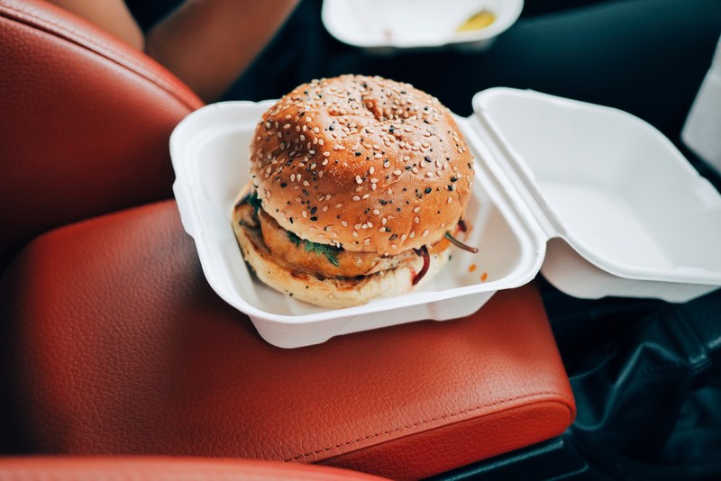 burger with a sesame bun in a styrofoam container on the center console in a car, burger in a car 4k