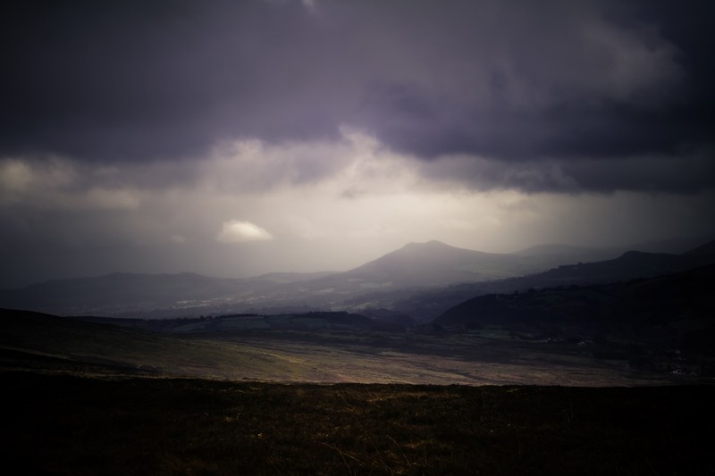 a dim shot of plains stretching to the low mountains on the horizon under gray clouds, dark plains in the mountains 4k