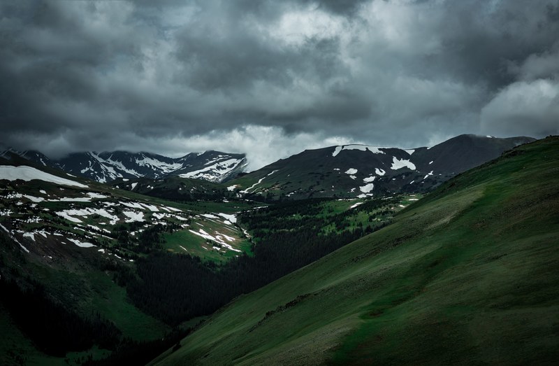 a green mountain valley with patches of snow under an overcast sky, gray skies over a wooded valley 4k