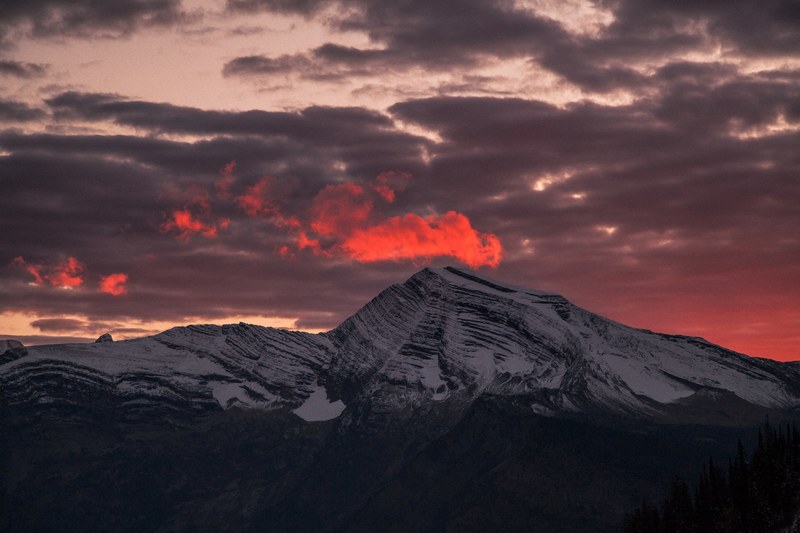 red clouds hang over a snowy mountain ridge as sun sets over west glacier, cold sunset 4k