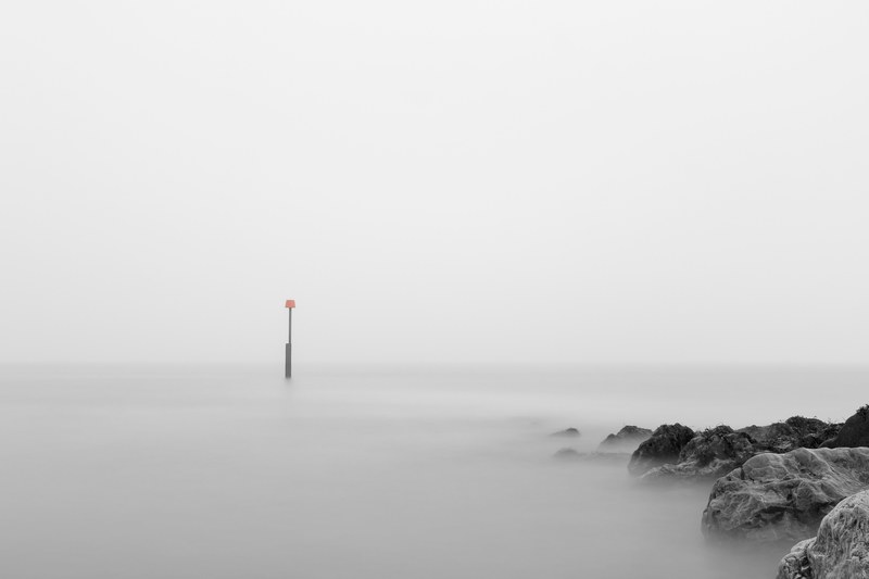 isolated sign in the middle of a foggy sea near rocks, reculver minimalist foggy seascape long exposure 4k