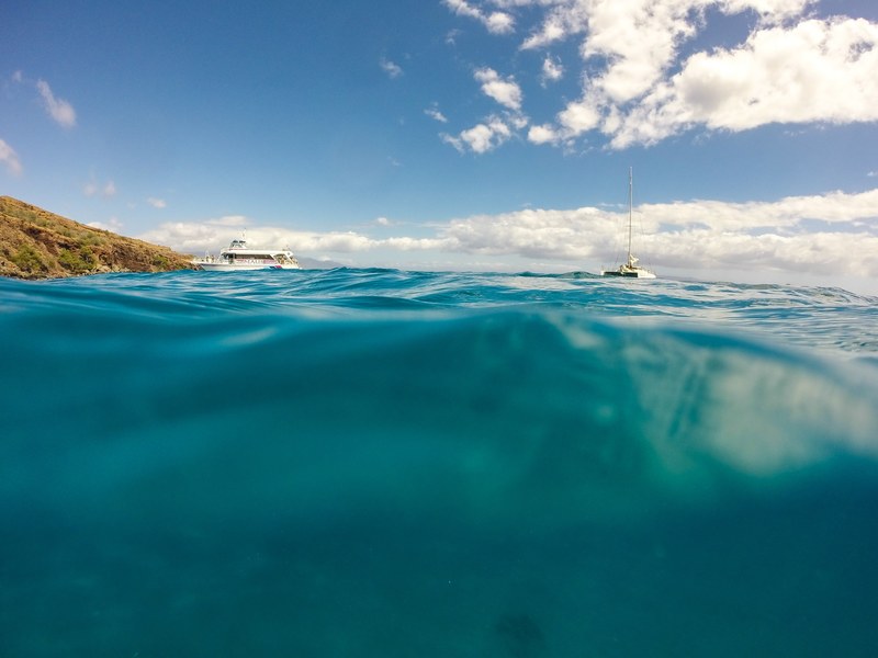 a yacht and a sailboat anchored in a bright blue ocean by a mountain, a yacht and a sailboat walk into a bar 4k