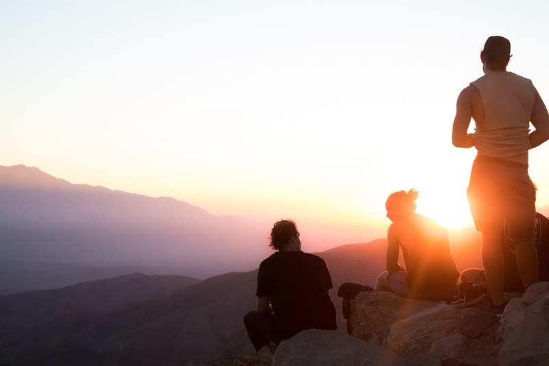 group hikers atop a rocky cliff taking a break by watching the sunset at joshua tree, joshua tree hikers resting 4k