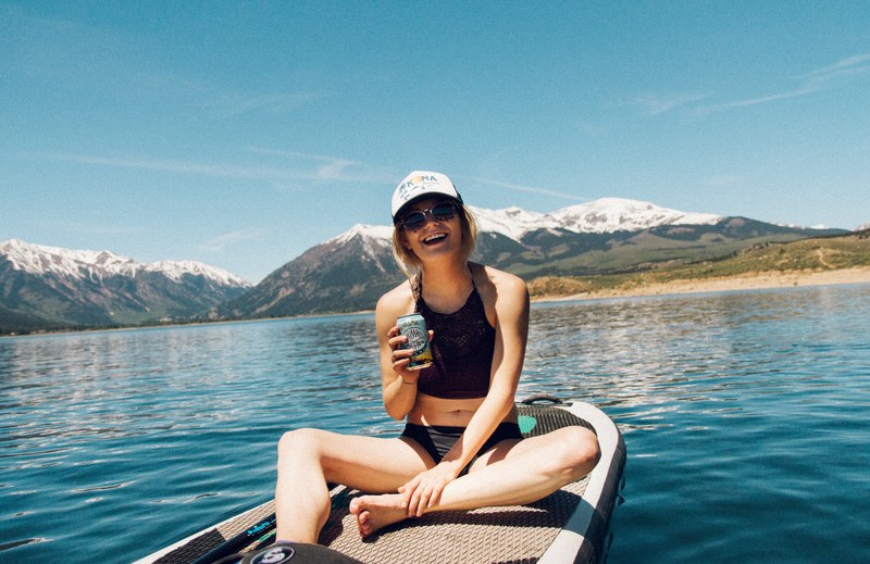 a woman sitting with a beer bottle and glass cups looking out the window of a bar while rain is falling, woman on paddle board 4k