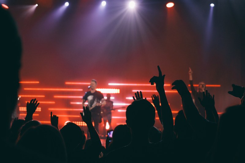 silhouettes of audience members in front of a stage with musicians under floodlights, first row at a concert 4k