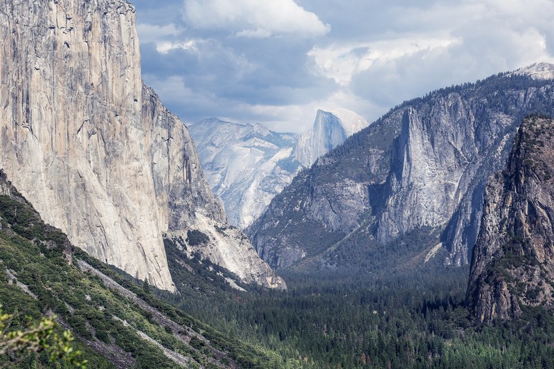 mountain landscape with lush trees in the valley and rocky hillsides, yosemite under clouds 4k