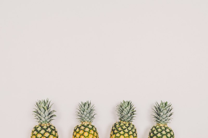 four pineapples arranged in a row against a white wall, four pineapples 4k
