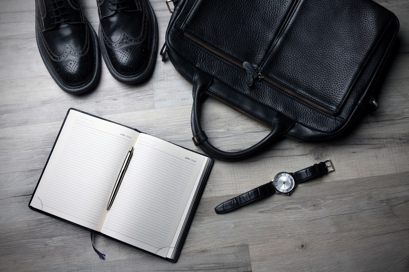 an overhead shot of a leather bag a pair of leather shoes and a watch next to an open notebook, black leather in flatlay 4k