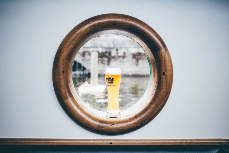 an alcohol glass cup on a porthole window with brown frame, glass cup on a window 4k