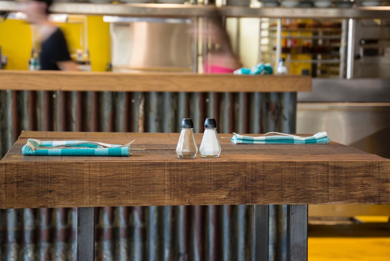 salt and pepper shakers on a wooden table with blue plaid napkins and a busy kitchen in the background, salt and pepper on table 4k