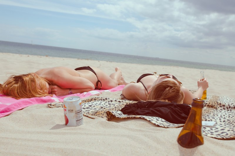 two young women in bikini enjoying sunbathing and tanning on the beach while drinking beer, _women sunbathing on beach 4k
