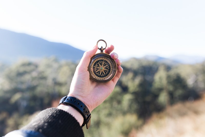 an outstretched hand holding a pocket compass with trees in the blurry background, explorers compass 4k