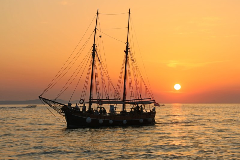 a sailboat on a tranquil sea as the sun sets in the distance, the sailboat and the sunset 4k