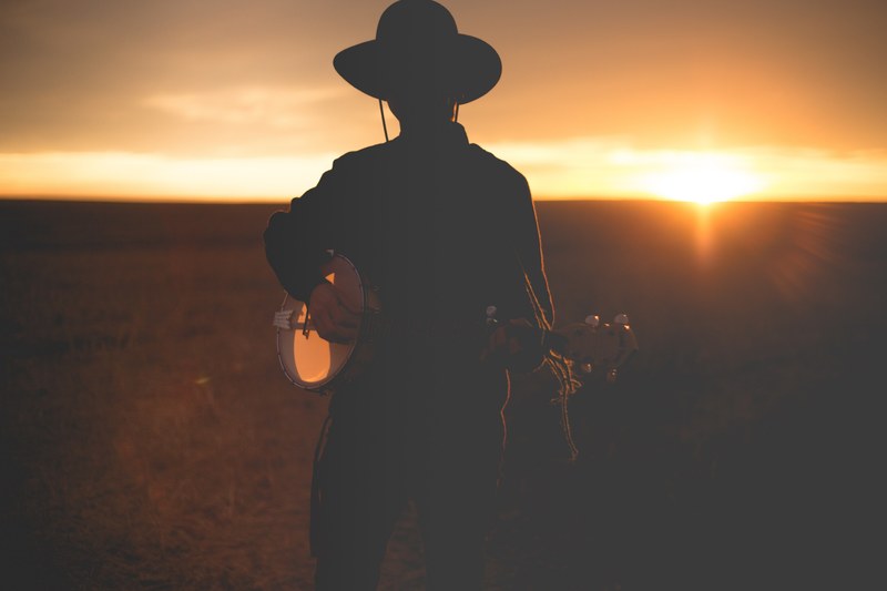 silhouette of musician with hat playing banjo in field during sunset, banjo player sunset 4k