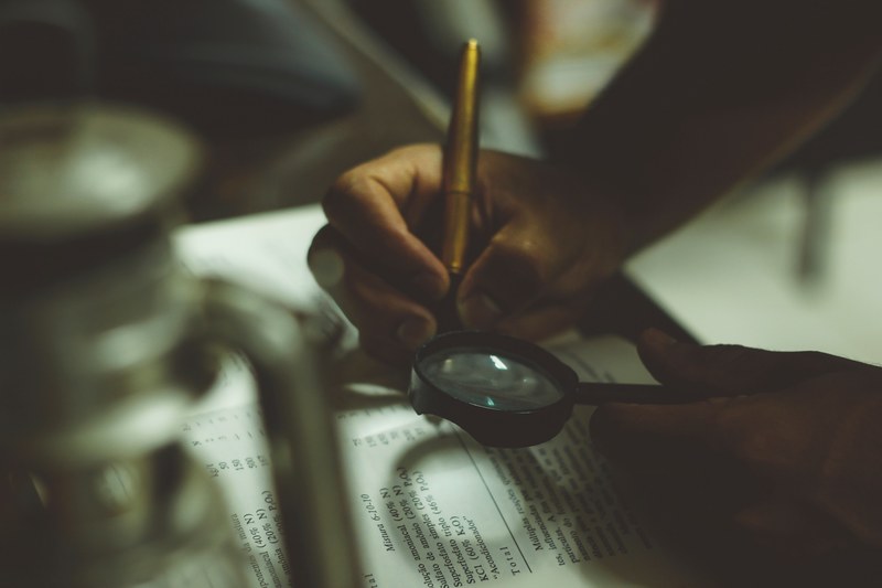 a person reading a book with a magnifying glass and a pen in hand, reading with magnifying glass 4k