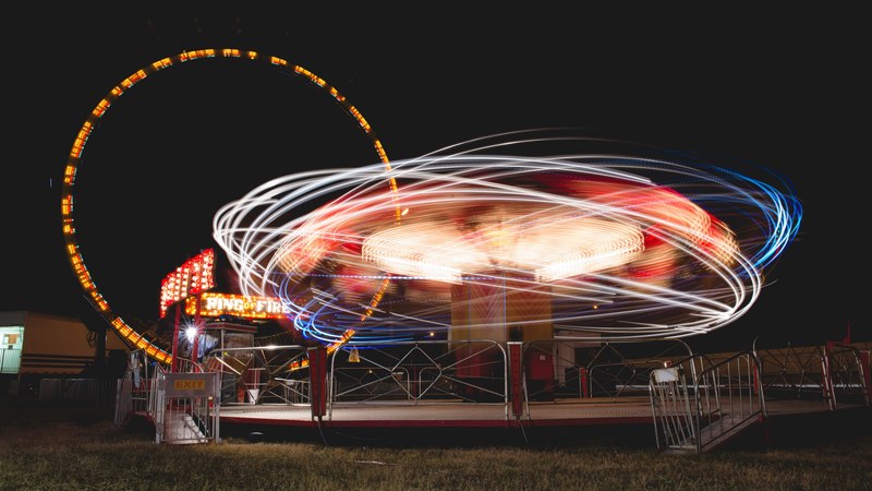 an eccentric lively image of illuminated carnival rides creating neon light trail patterns in various colors, neon light trails at fairground 4k