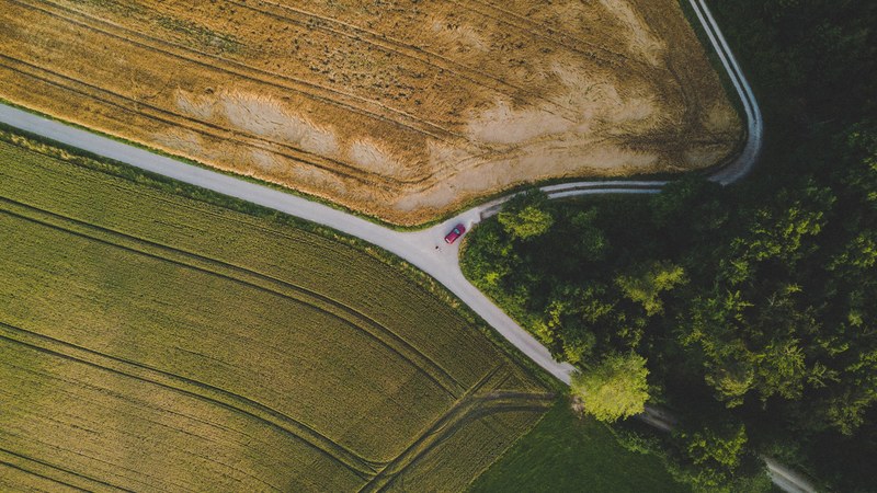 a drone shot of a car at a rural intersection surrounded by fields, separated land 4k