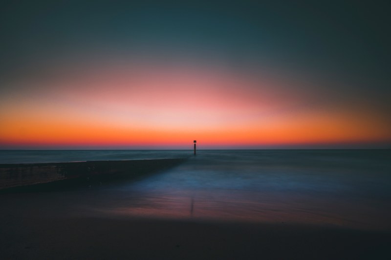 one silhouette pole in the calm smooth sea at bournemouth beach during sunrise or sunset coloring the dark sky orange, days by the beach 4k